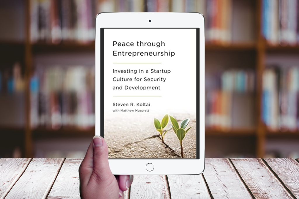 Hand holding a tablet displaying the cover of "Peace through Entrepreneurship" by Steven Koltai