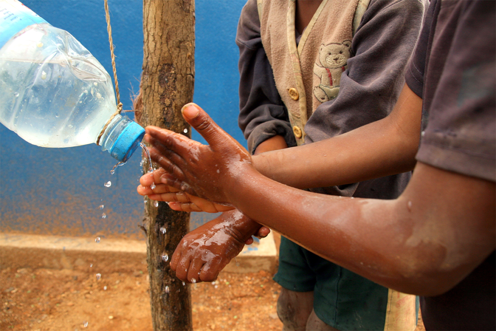 Hands of two Black children in Madagascar using a tippy tap handwashing tool