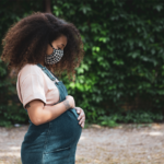 Black woman wearing a face mask cradles her pregnant torso