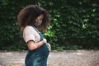 Black woman wearing a face mask cradles her pregnant torso