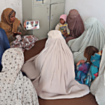 Community health worker in Afghanistan holds a tablet showing a reproductive health video to a small group of women wearing traditional Islamic dress