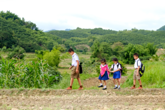 Four young siblings wearing school uniforms walk across a crop field