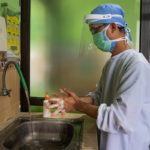 Health care worker in Indonesia washes his hands with soap while dressed in scrubs, face shield and face mask