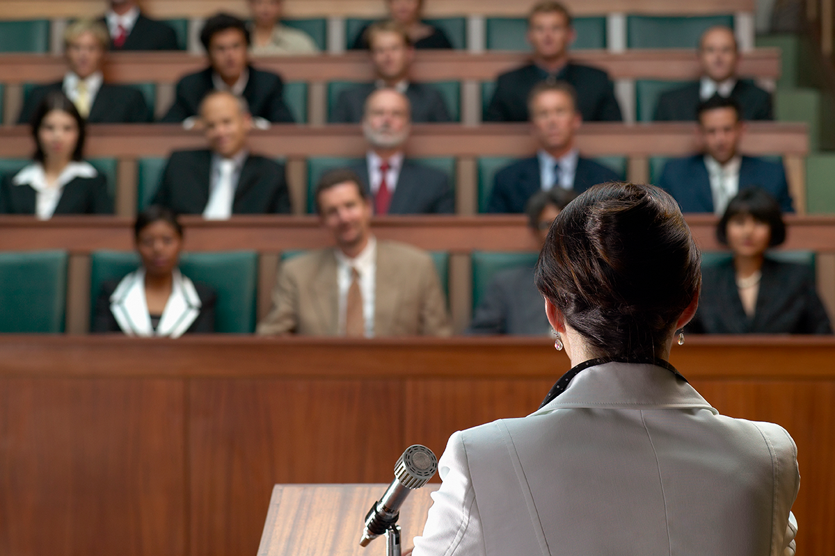 Rear view of woman standing at a podium speaking to an audience