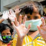 A masked child holding up soapy hands