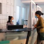 Woman talks to a clinical office receptionist through COVID protection glass