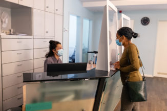 Woman talks to a clinical office receptionist through COVID protection glass