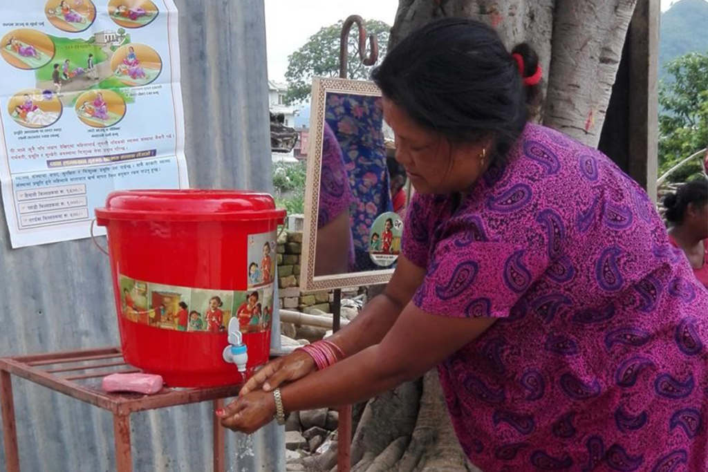 Woman washing her hands under the nozzle of a red bucket