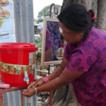 Woman washing her hands under the nozzle of a red bucket